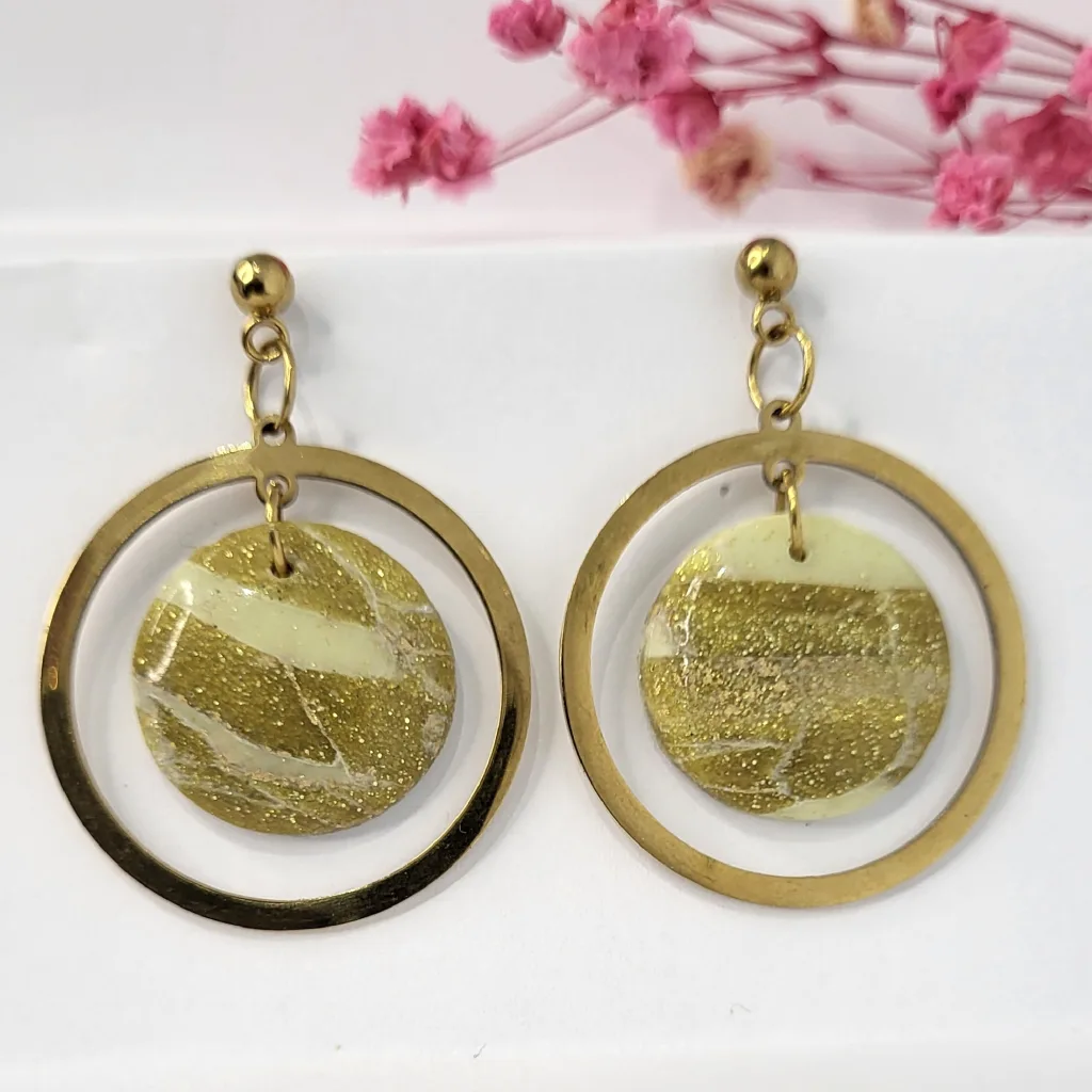 Boucles d'oreilles pendantes artisanales en pâte polymère marbrée vert-or et résine, montées sur des anneaux et tiges en acier inoxydable doré.