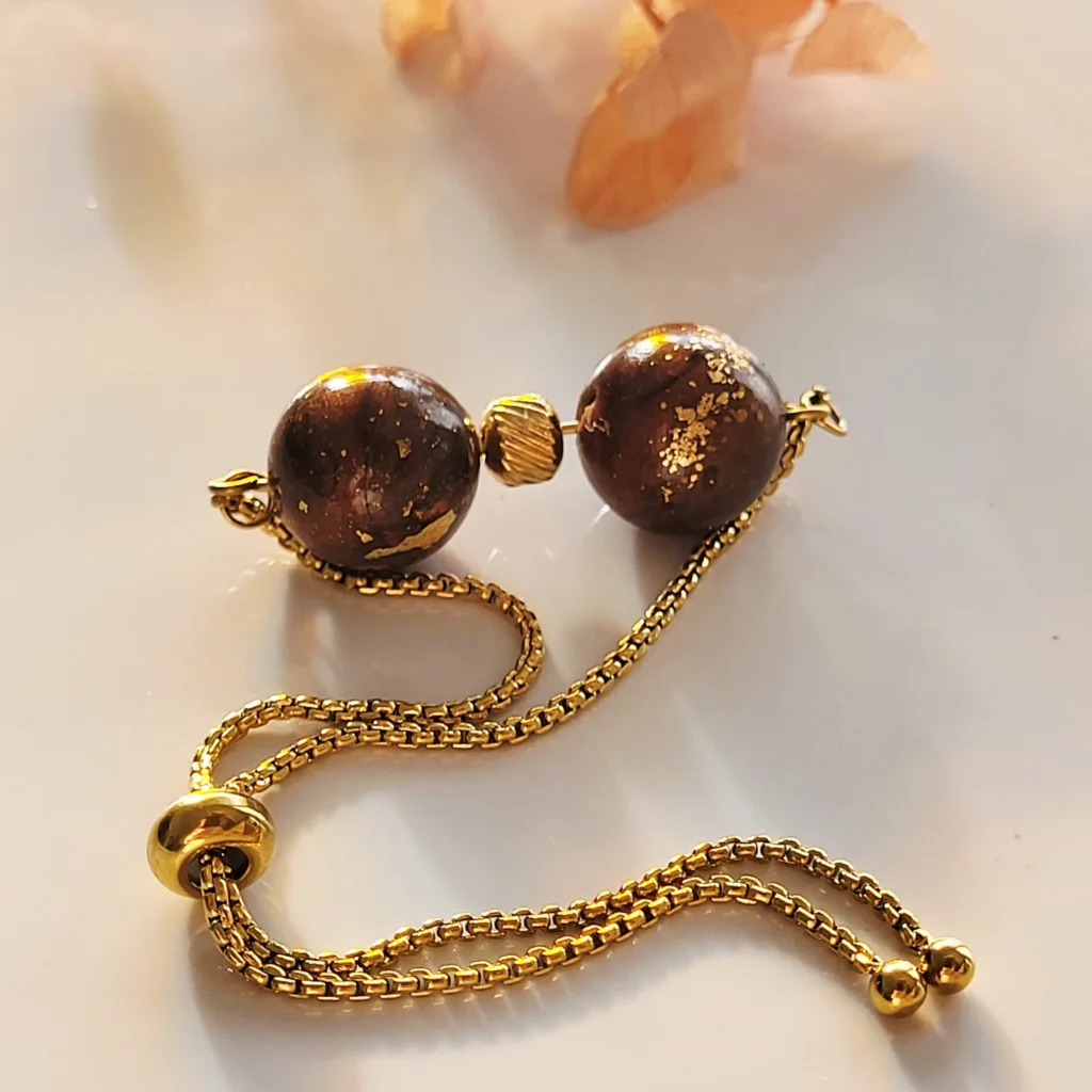 Bracelet ajustable en acier inoxydable doré avec deux perles artisanales en pâte polymère marron effet marbré et feuilles d'or.