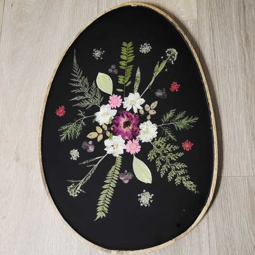 Plateau ovale artisanal en bois de manguier avec inclusion de fleurs séchées blanches et roses dans de la résine noire.