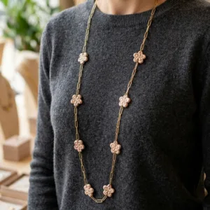 Sautoir fleurs artisanales rose et doré Sautoir artisanal en acier inoxydable PVD doré avec petites fleurs en pâte polymère résine rose poudré porté par une femme.