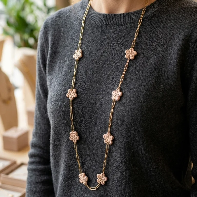 Sautoir artisanal en acier inoxydable PVD doré avec petites fleurs en pâte polymère résine rose poudré porté par une femme.