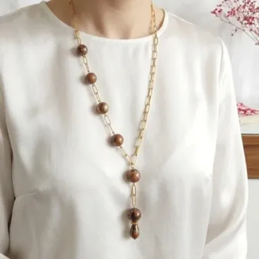 Collier cravate artisanal pour femme avec pampille de perles marbrées brunes et inclusions dorées sur chemise blanche