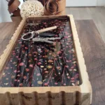 Grand vide-poche rectangulaire en bois et résine artisanale avec inclusions de fleurs séchées roses et or, style bohème chic, posé sur une table en bois avec clés.