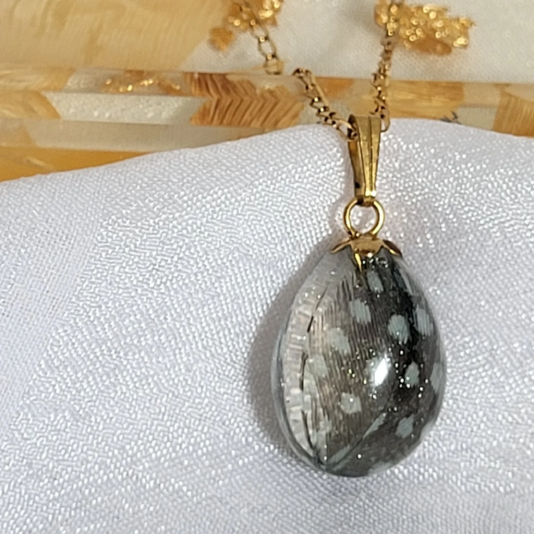 Collier artisanal en acier inoxydable chirurgical avec placage PVD or, pendentif goutte résine et plume naturelle.