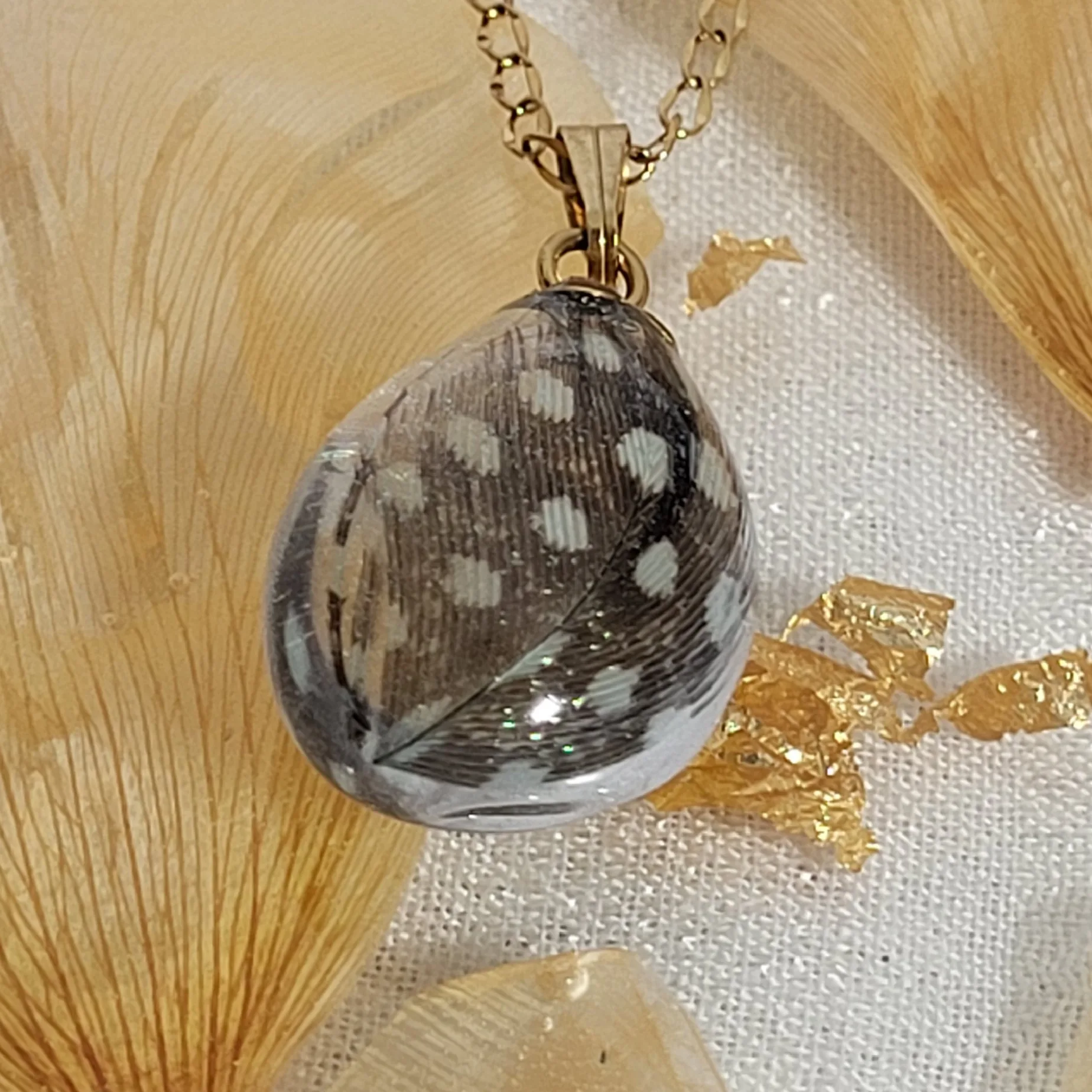 Collier artisanal en acier inoxydable chirurgical avec placage PVD or, pendentif goutte résine et plume naturelle.