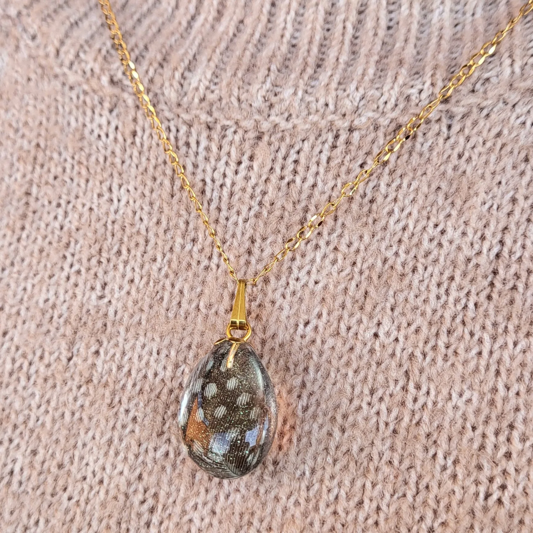 Collier artisanal en acier inoxydable chirurgical avec placage PVD or, pendentif goutte résine et plume naturelle.