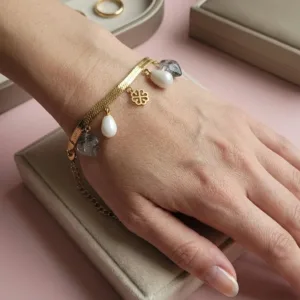 Bracelet doré maille serpent avec breloques en résine, perles blanches et pendentif trèfle, porté au poignet