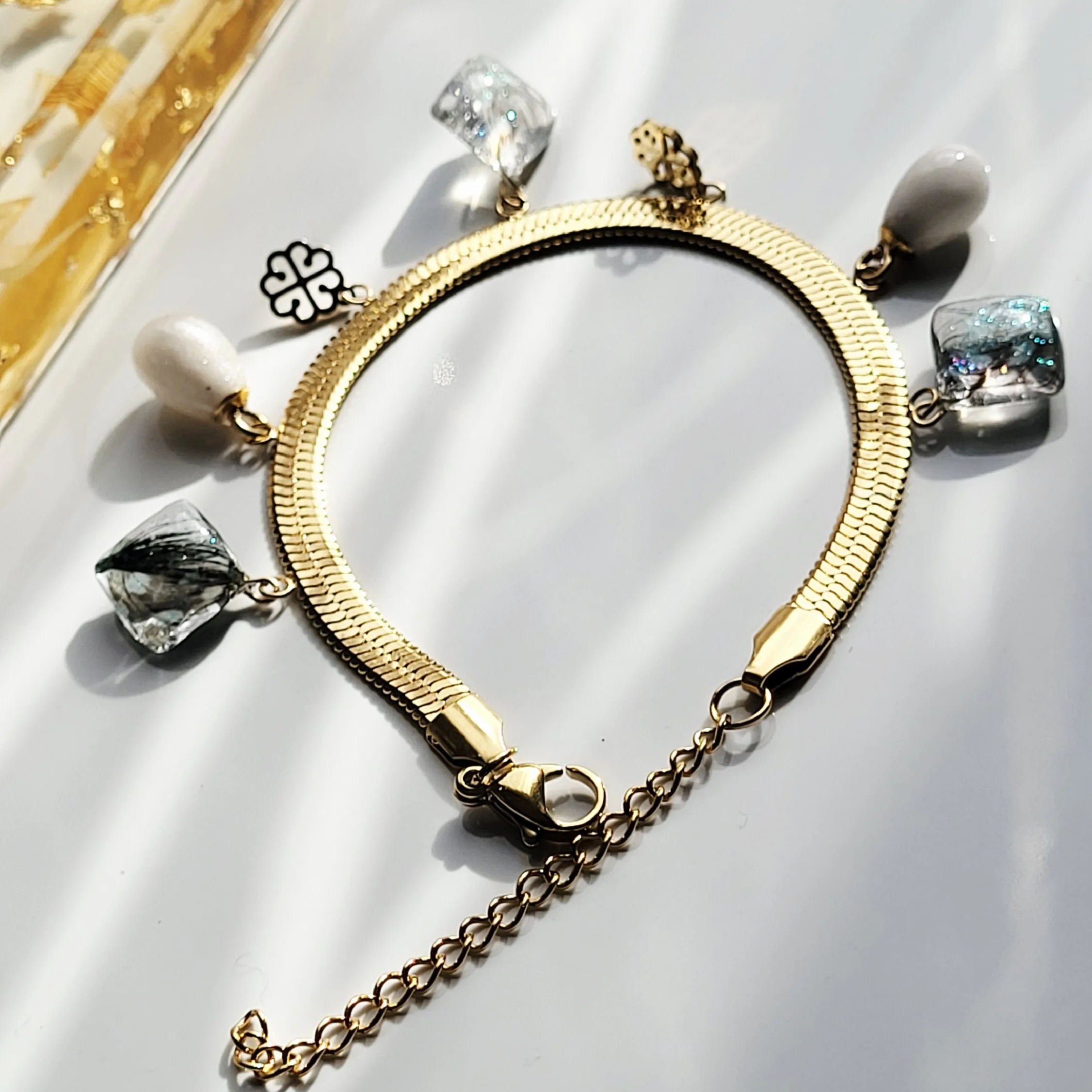 Bracelet artisanal Inaya en acier inoxydable doré avec véritable plume naturelle et trèfle en nacre.