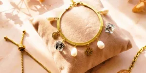 Gros plan sur un bracelet de la Collection Fleurs et Résine, présentant des inclusions de fleurs séchées jaune doré dans des perles transparentes. Assemblage sur fil métallique et chaînette d'extension en métal doré. Arrière-plan flou d'une petite fleur jaune séchée, sous lumière naturelle chaude.