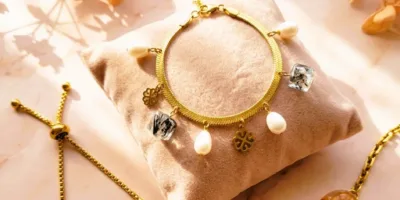 Gros plan sur un bracelet de la Collection Fleurs et Résine, présentant des inclusions de fleurs séchées jaune doré dans des perles transparentes. Assemblage sur fil métallique et chaînette d'extension en métal doré. Arrière-plan flou d'une petite fleur jaune séchée, sous lumière naturelle chaude.