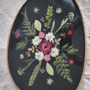 Plateau ovale artisanal en bois de manguier avec inclusion de fleurs séchées blanches et roses dans de la résine noire.