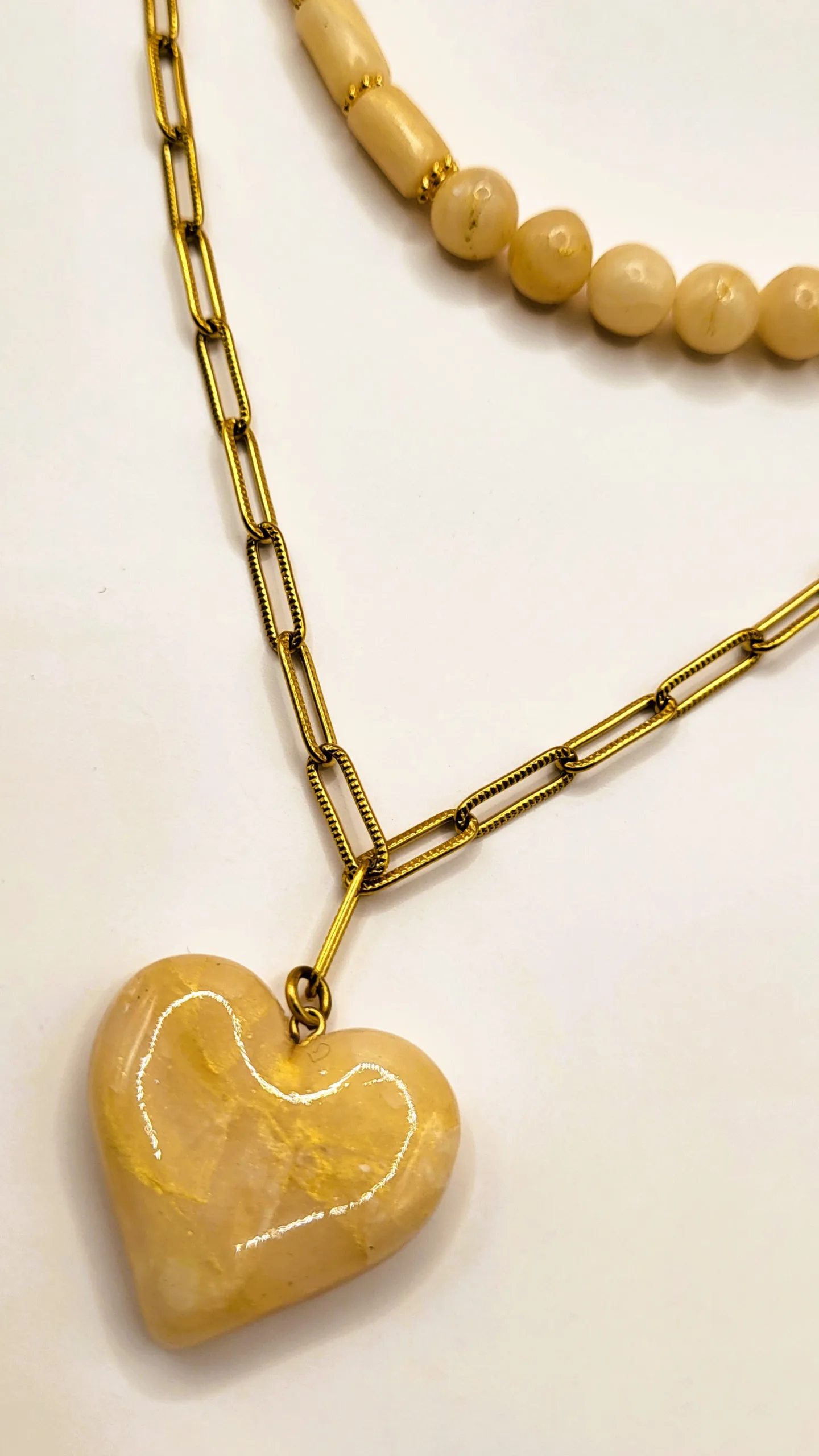 Détail du pendentif cœur en pâte polymère marbrée beige et or, suspendu à une fine chaîne dorée en maille rectangulaire.