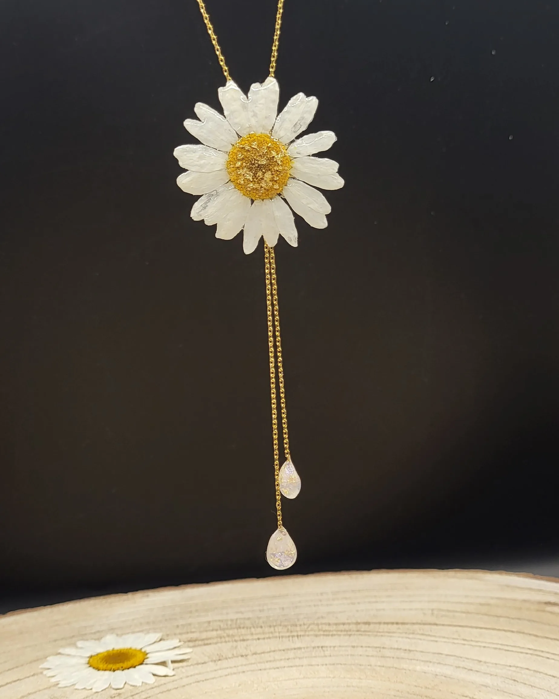 Collier marguerite en résine présenté sur un support en bois naturel.