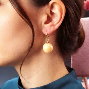 Femme portant des boucles d'oreilles pendantes avec une perle ronde crème et une attache dorée.