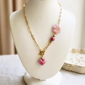 Collier artisanal composé d'un pendentif cœur en pâte polymère et une fleur séchée sur une chaîne en acier inoxydable 316L doré, présenté sur un buste de mannequin.